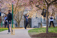 Students cheer while playing a game of cricket on a spring day.